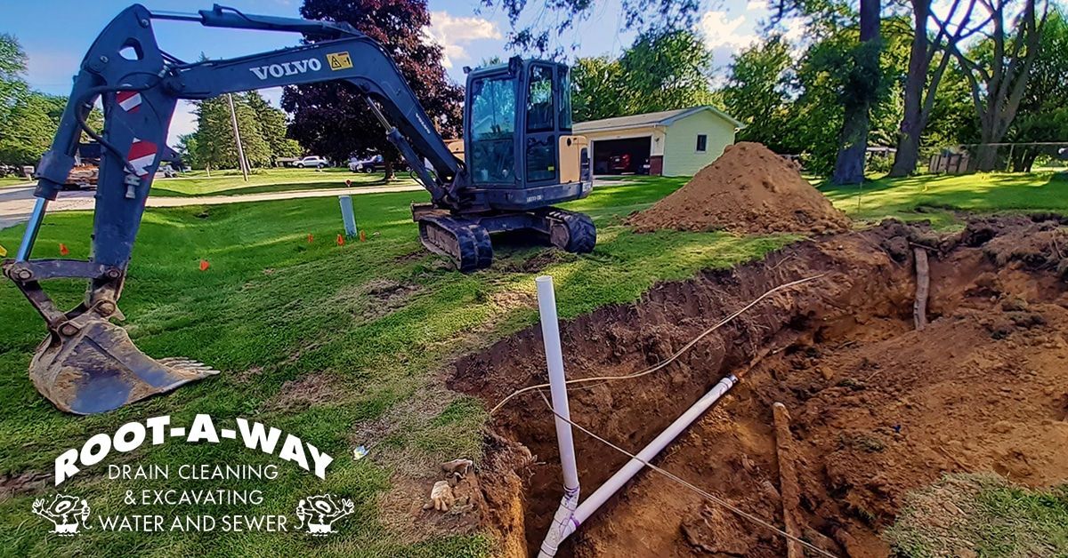 Excavator digging a trench beside a white pipe in a grassy yard Excavator digging a trench beside a white pipe in a grassy yard