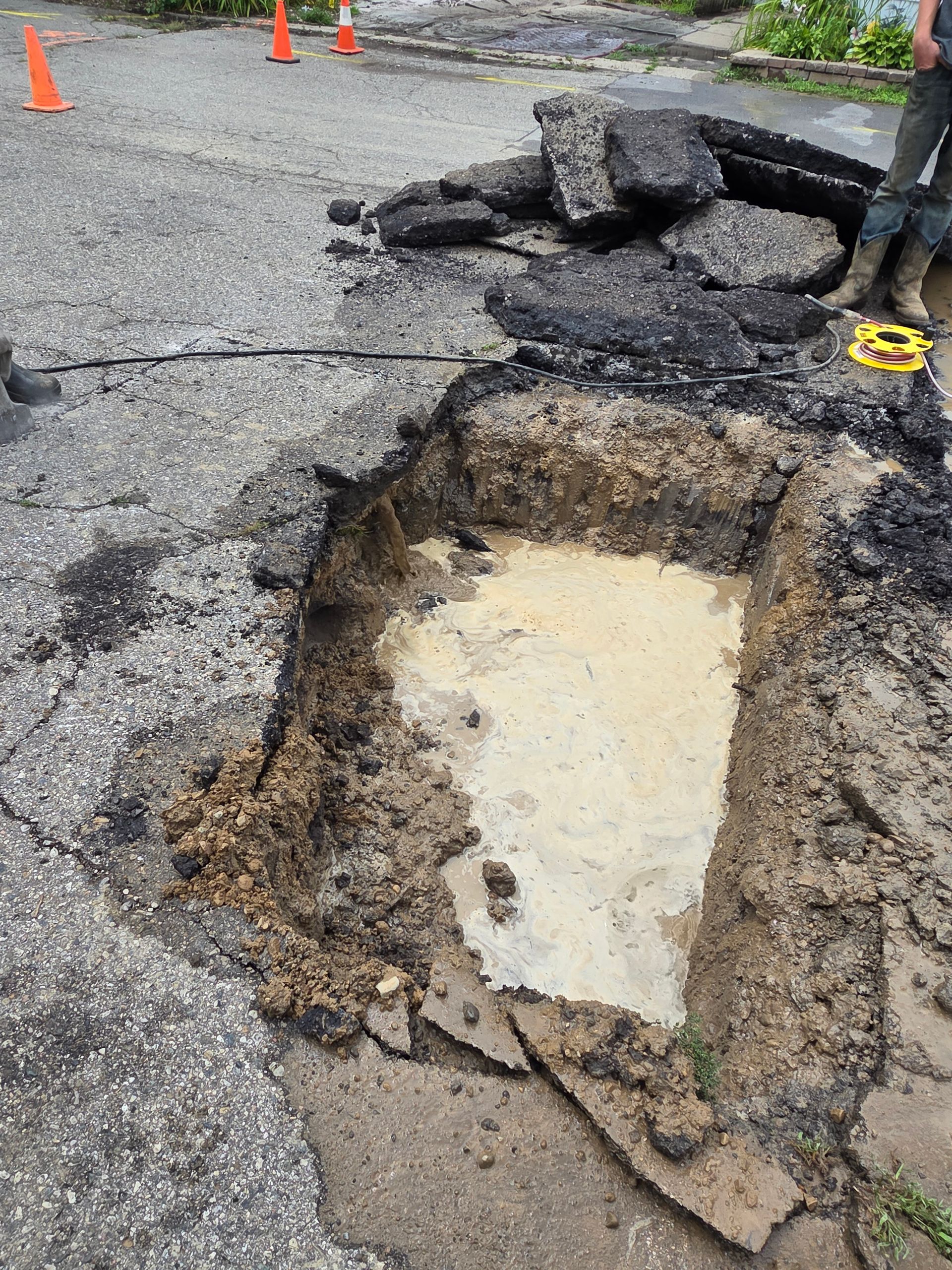 Large pothole in cracked road with exposed base and piled asphalt debris nearby