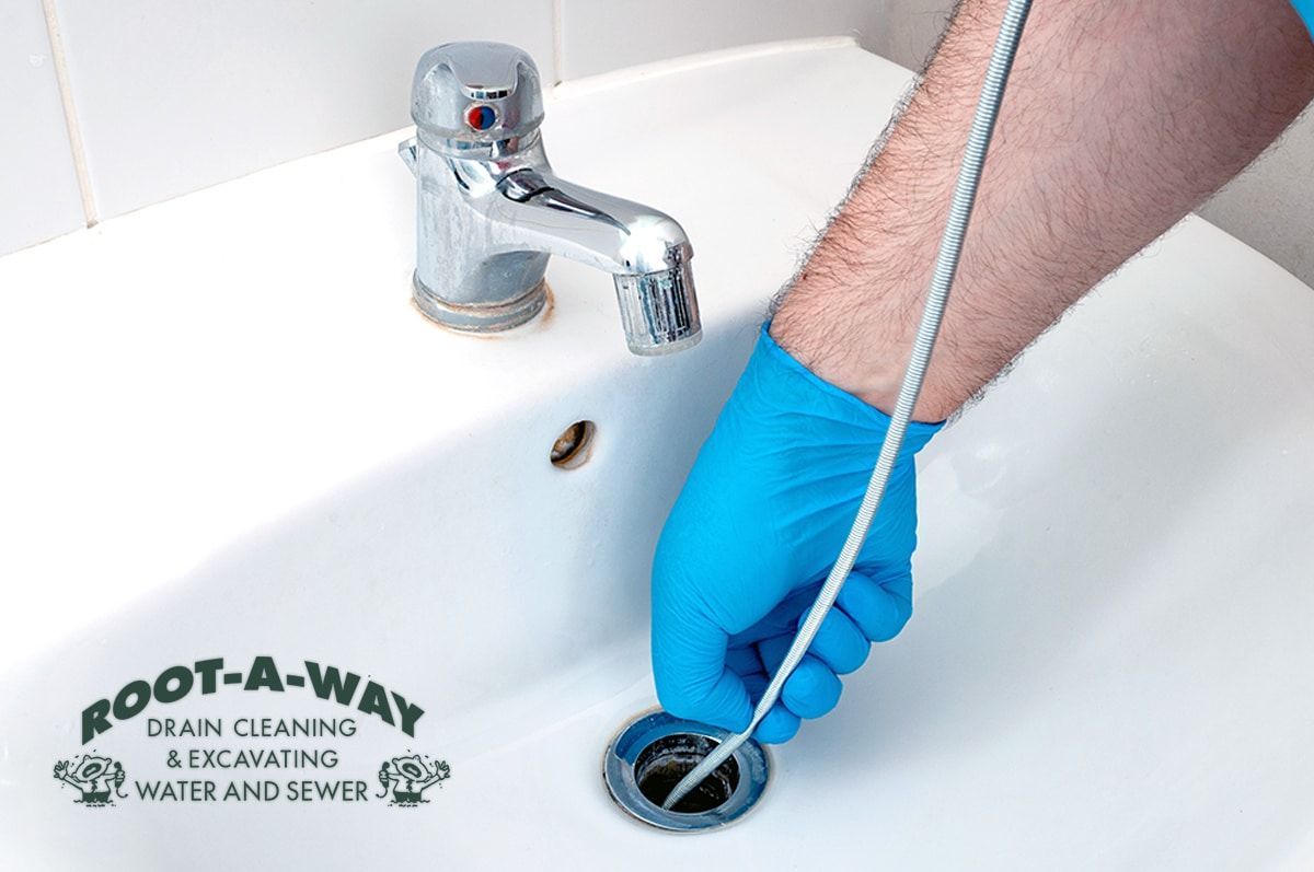 Blue-gloved hand cleaning a sink drain with a flexible brush