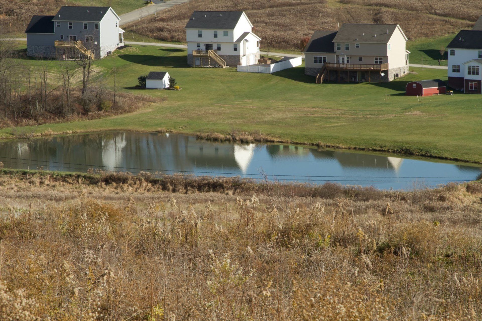 A small pond in the middle of a field with houses in the background
