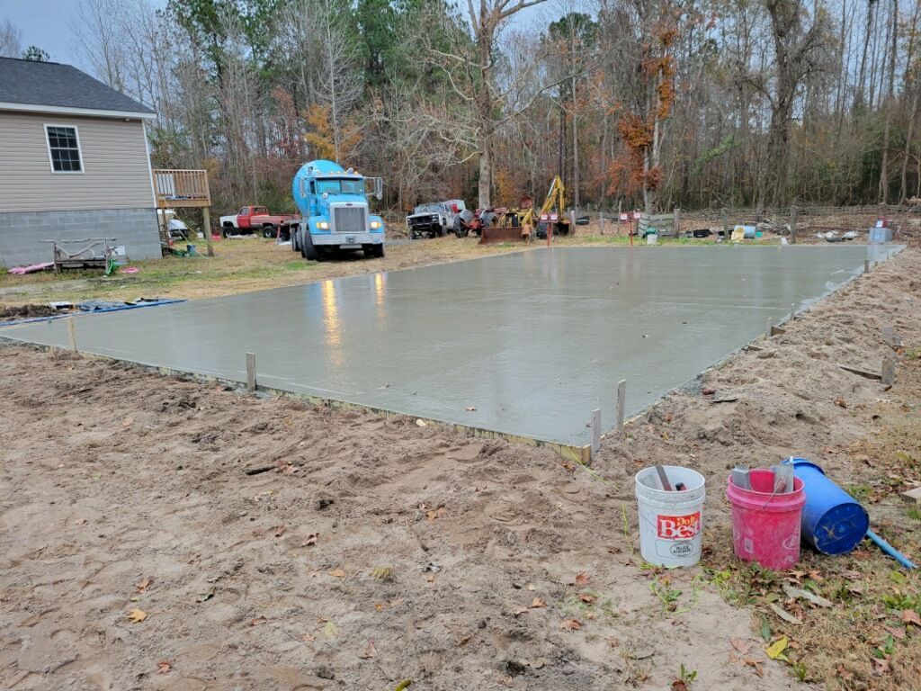 Freshly poured concrete slab beside a house, with a blue mixer truck and tools nearby