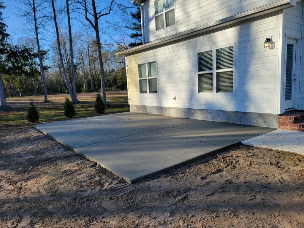 Concrete service crew pouring and finishing new slab. Concrete patio beside a white house under construction, with windows and bare yard around it