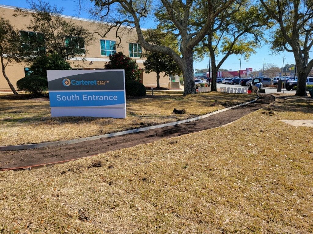 South Entrance sign outside a beige building with trees and parked cars nearby.