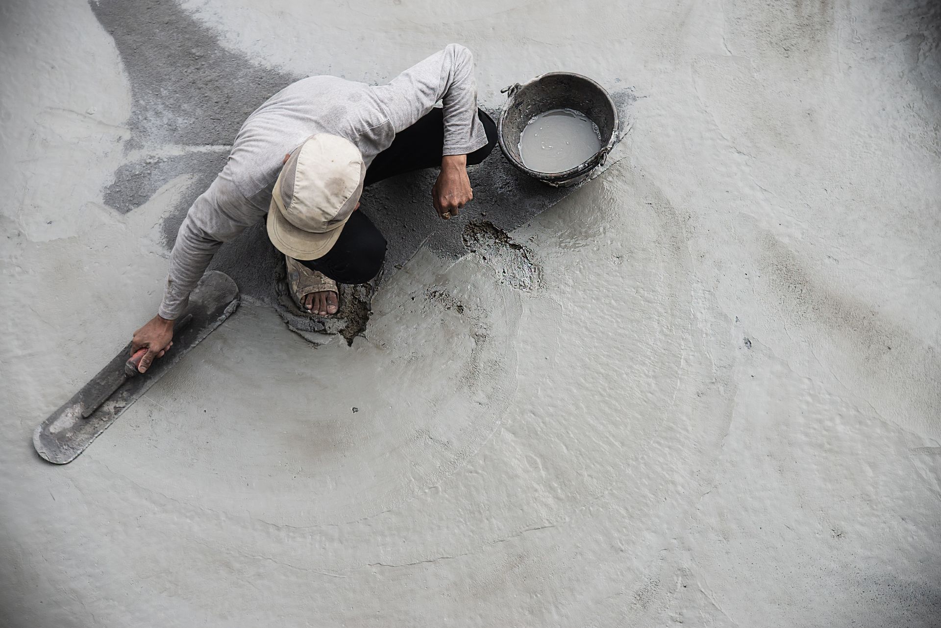 Worker from a local concrete contractor finishing a damp cement foundation with precision tools.