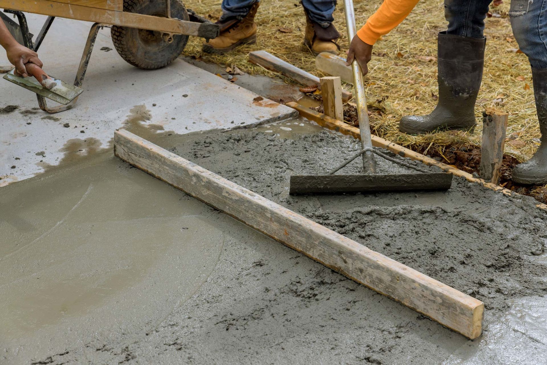 Workers smoothing wet concrete with a screed and shovel at a construction site