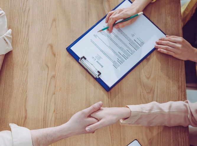 A woman is signing a document on a clipboard while a man shakes her hand.