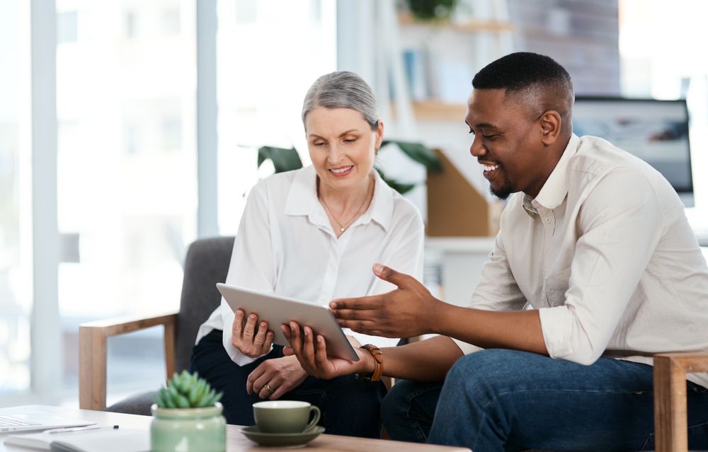 A man and a woman are sitting on a couch looking at a tablet.
