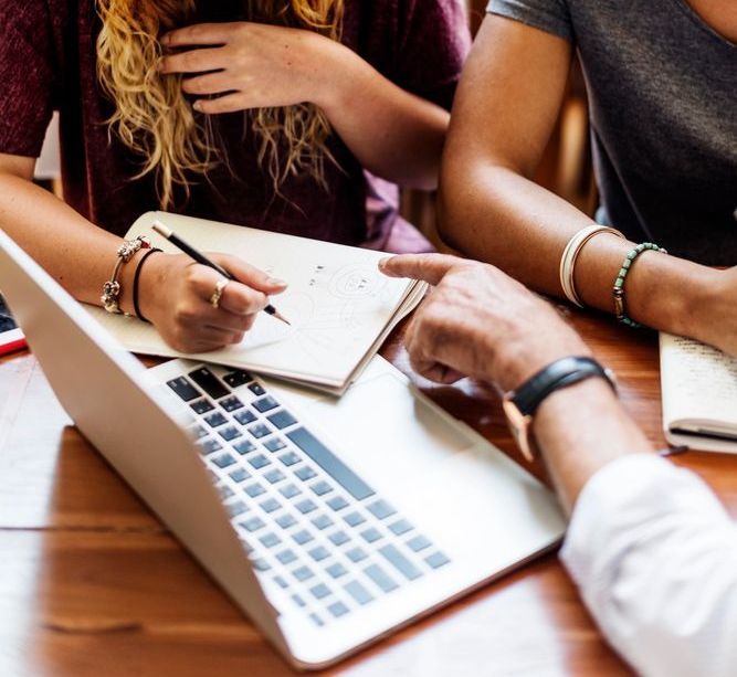 A group of people are sitting at a table with a laptop and notebooks