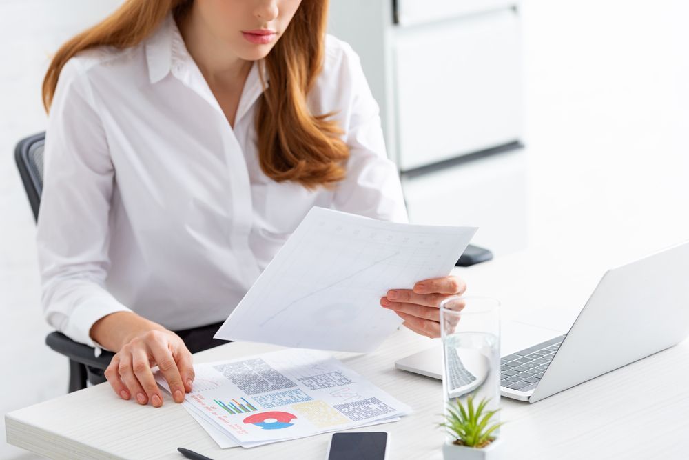 A woman is sitting at a desk looking at a piece of paper.