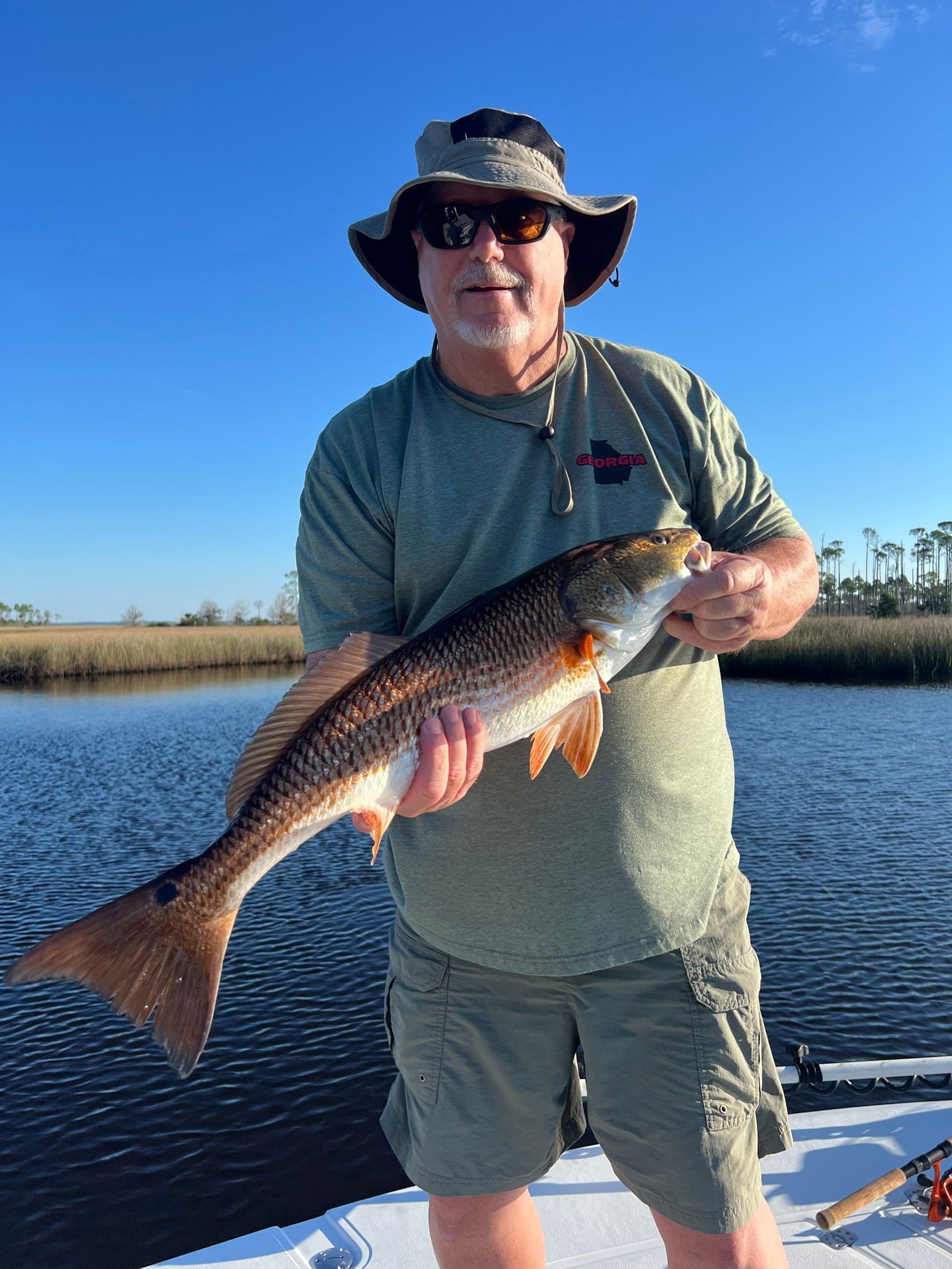 A man is standing on a boat holding a large red fish.