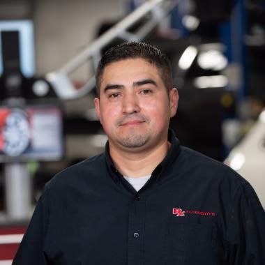 Man in a black work shirt at an auto shop, smiling at the camera. | RX Automotive