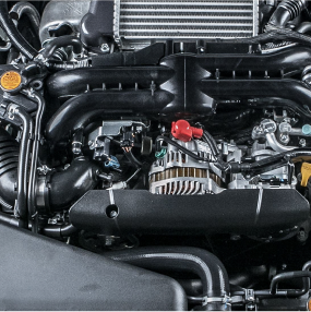 Close-up of a black car engine with various pipes, wires, and a prominent alternator. The engine is in a vehicle. | RX Automotive
