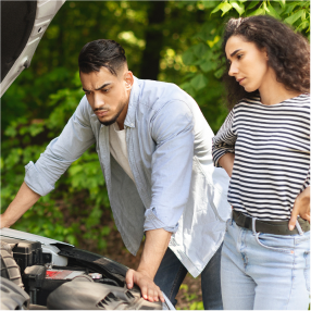 Man in light blue shirt inspects car engine, concerned expression. Woman watches, wearing striped shirt and jeans. Forest background. | RX Automotive