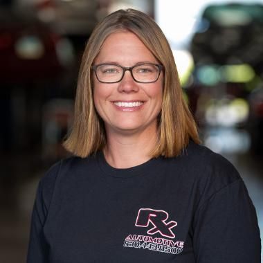 A woman with glasses and a black shirt smiling. She's in an auto repair shop. | RX Automotive