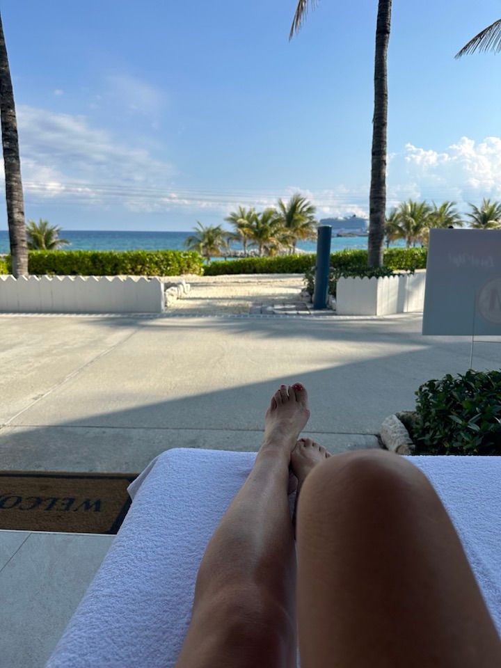 Relaxing feet by a resort pool with ocean and palm trees in the background