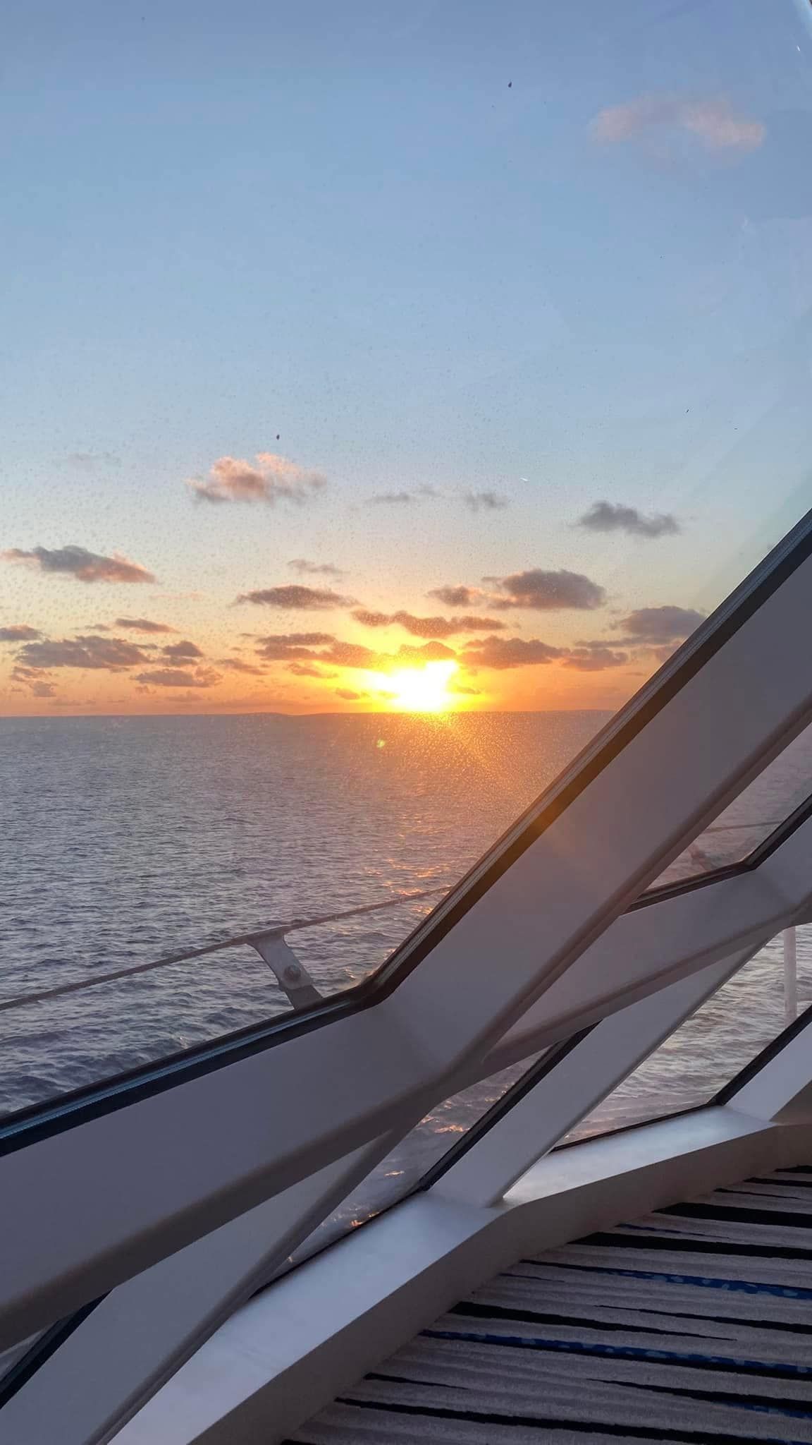 Sunset over the ocean, viewed from a ship deck with angular railings in the foreground