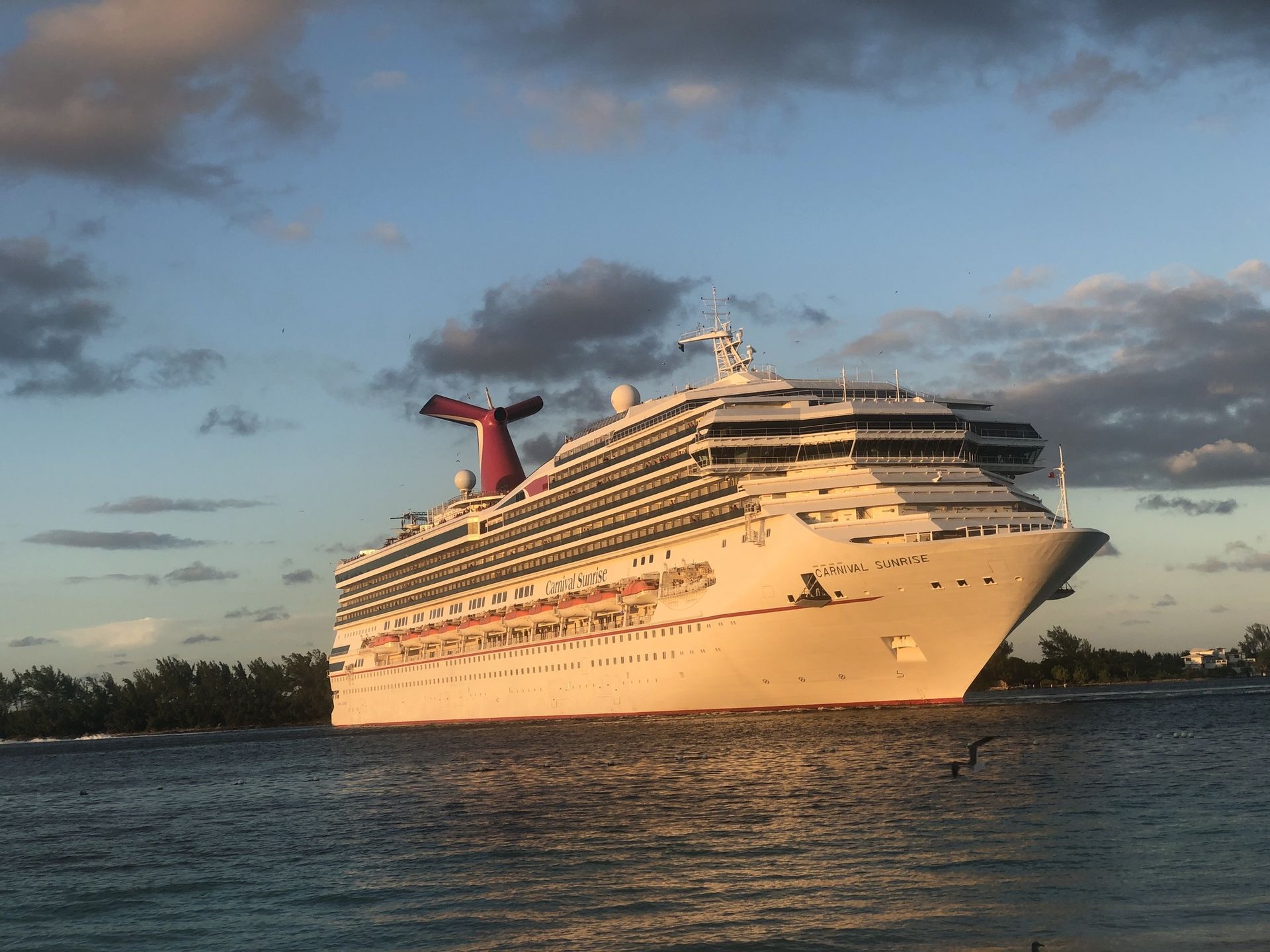 Large white cruise ship at sunset on calm water, with a red funnel and cloudy sky
