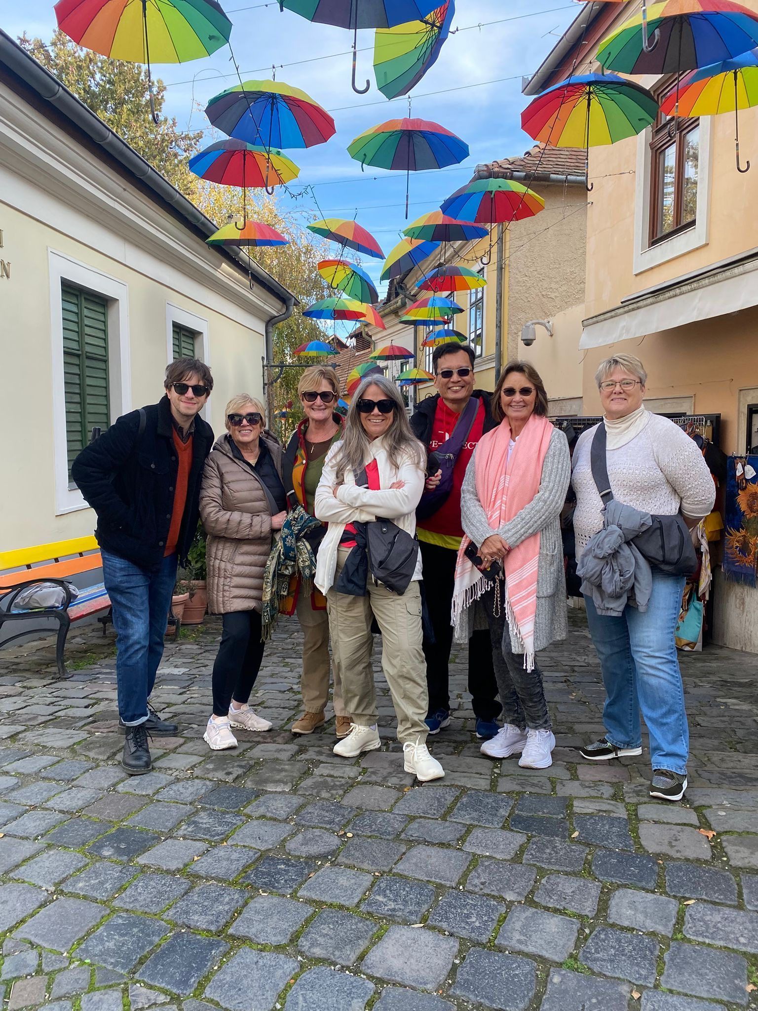 Group posing under colorful umbrellas on a cobblestone street in a narrow village alley
