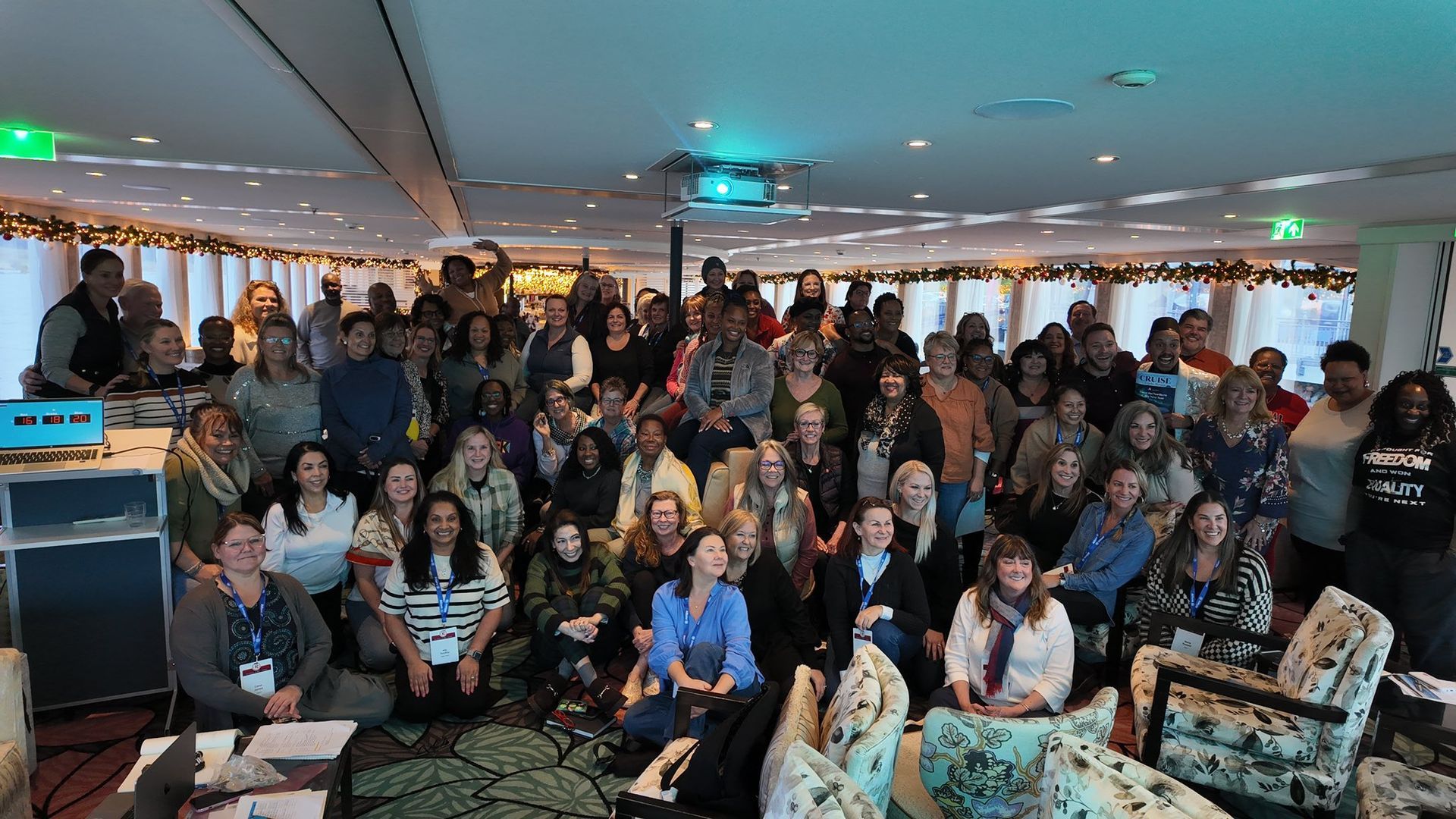 Large group posing for a photo in a bright indoor event space with tables and chandeliers.