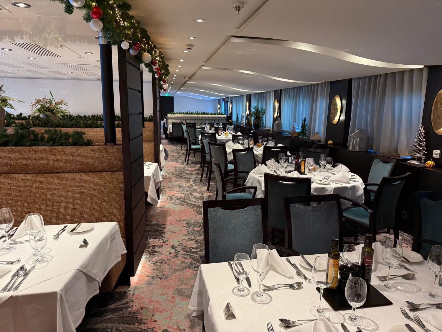 Elegant banquet dining room with set tables, black chairs, white linens, and holiday garland along the ceiling
