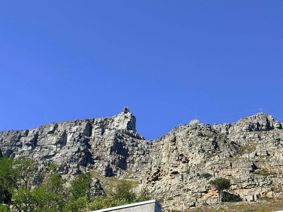 Rocky mountain cliff under a clear blue sky with sparse green trees at the base