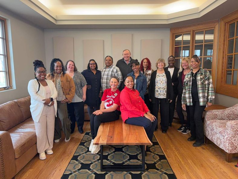 Group of people posing in a living room, with two women seated on a coffee table in front.