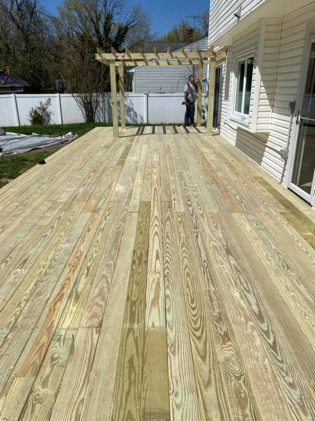 A man is standing on a wooden deck in front of a house.