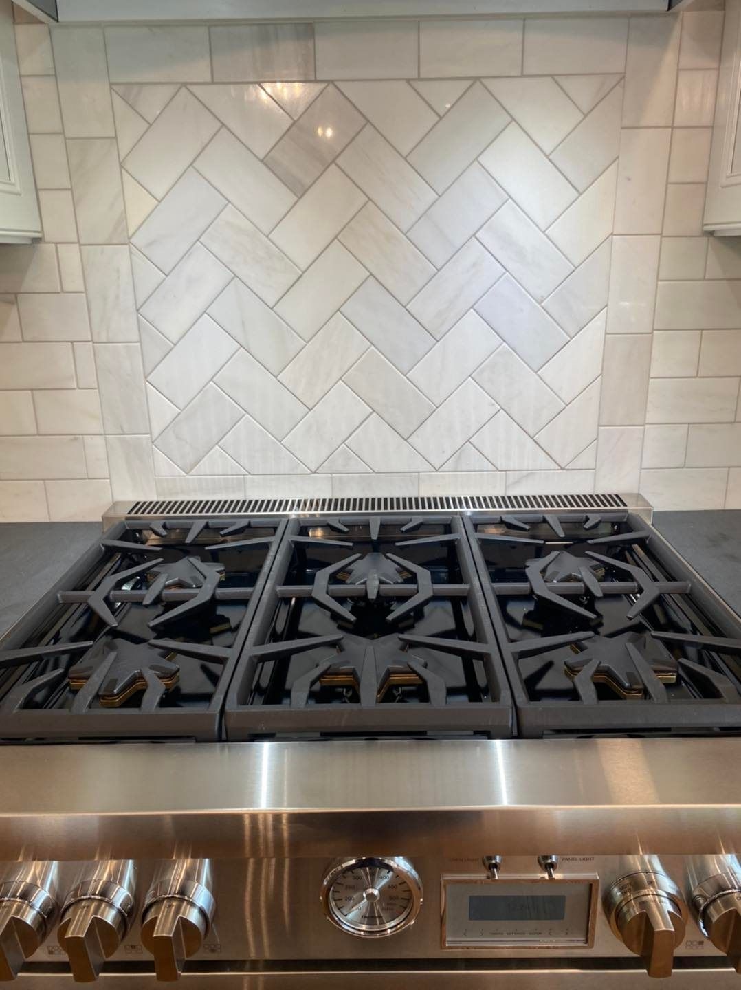 A stainless steel stove top oven with a herringbone tile backsplash.