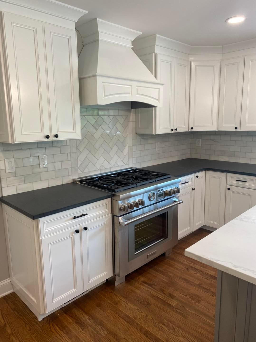 A kitchen with white cabinets , stainless steel appliances , and black counter tops.