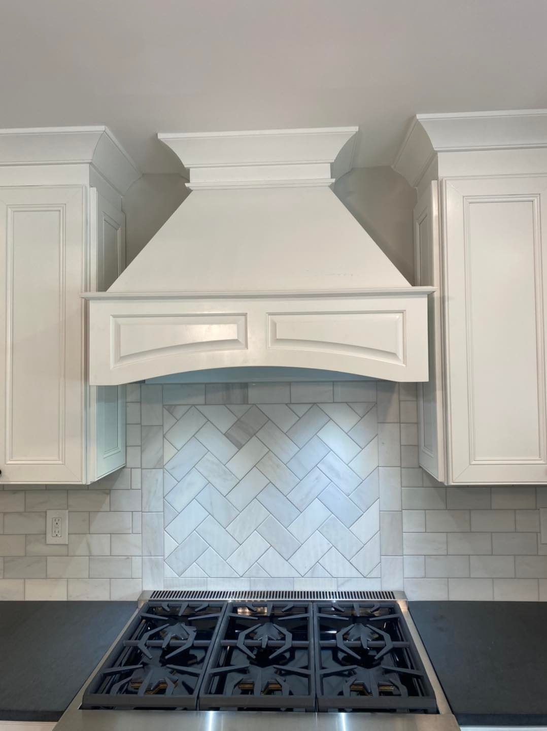 A kitchen with white cabinets and a stove top oven with a hood above it.