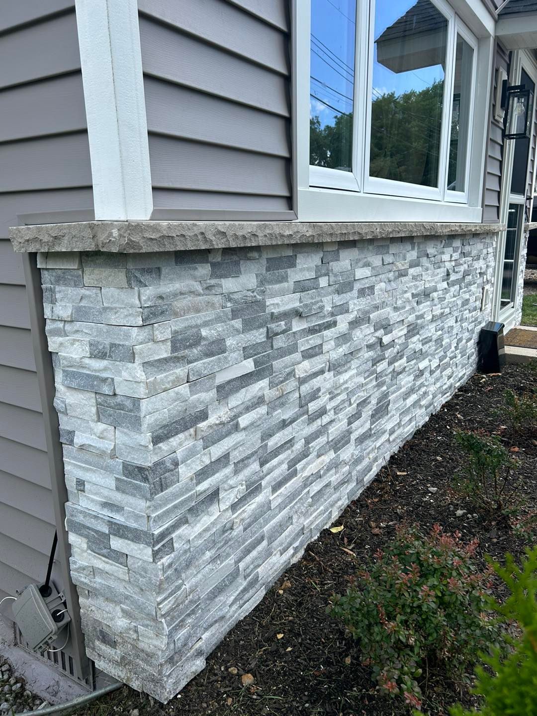 The side of a house with a stone wall and a window.