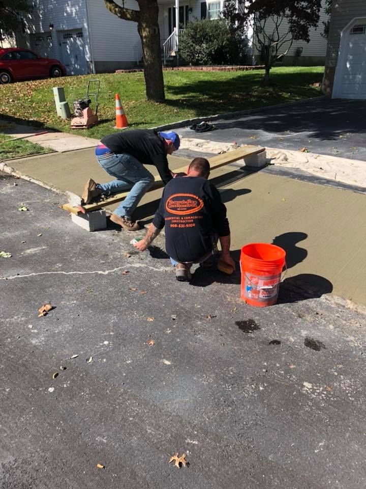 Two men are working on a sidewalk in a driveway.