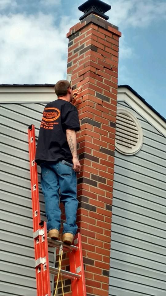 A man standing on a ladder next to a brick chimney