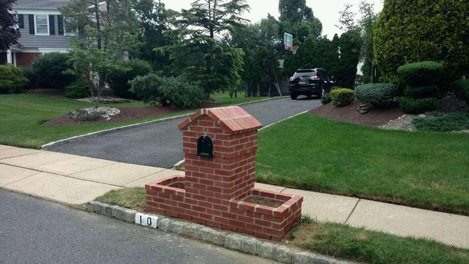 A brick mailbox is sitting on the sidewalk in front of a house.