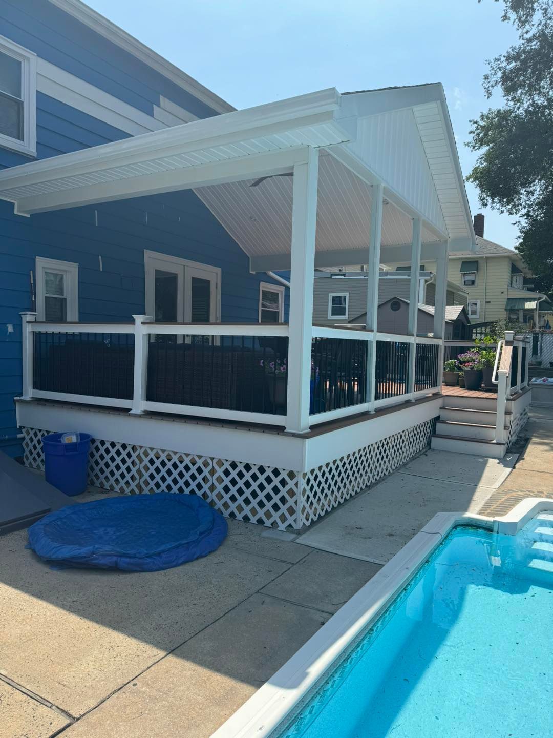 A blue house with a white porch and a pool in front of it.