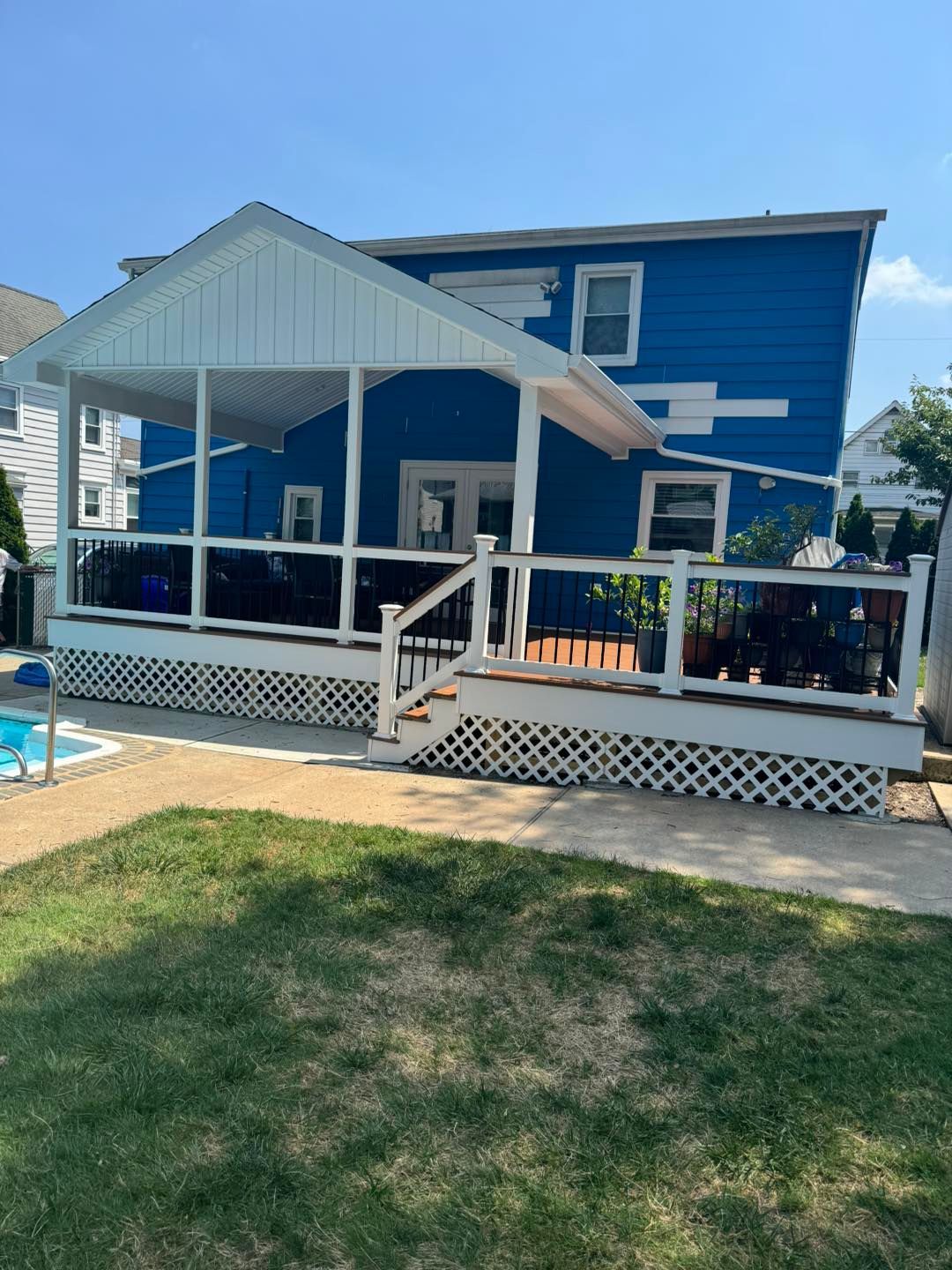 A blue house with a white porch and a pool in the backyard.