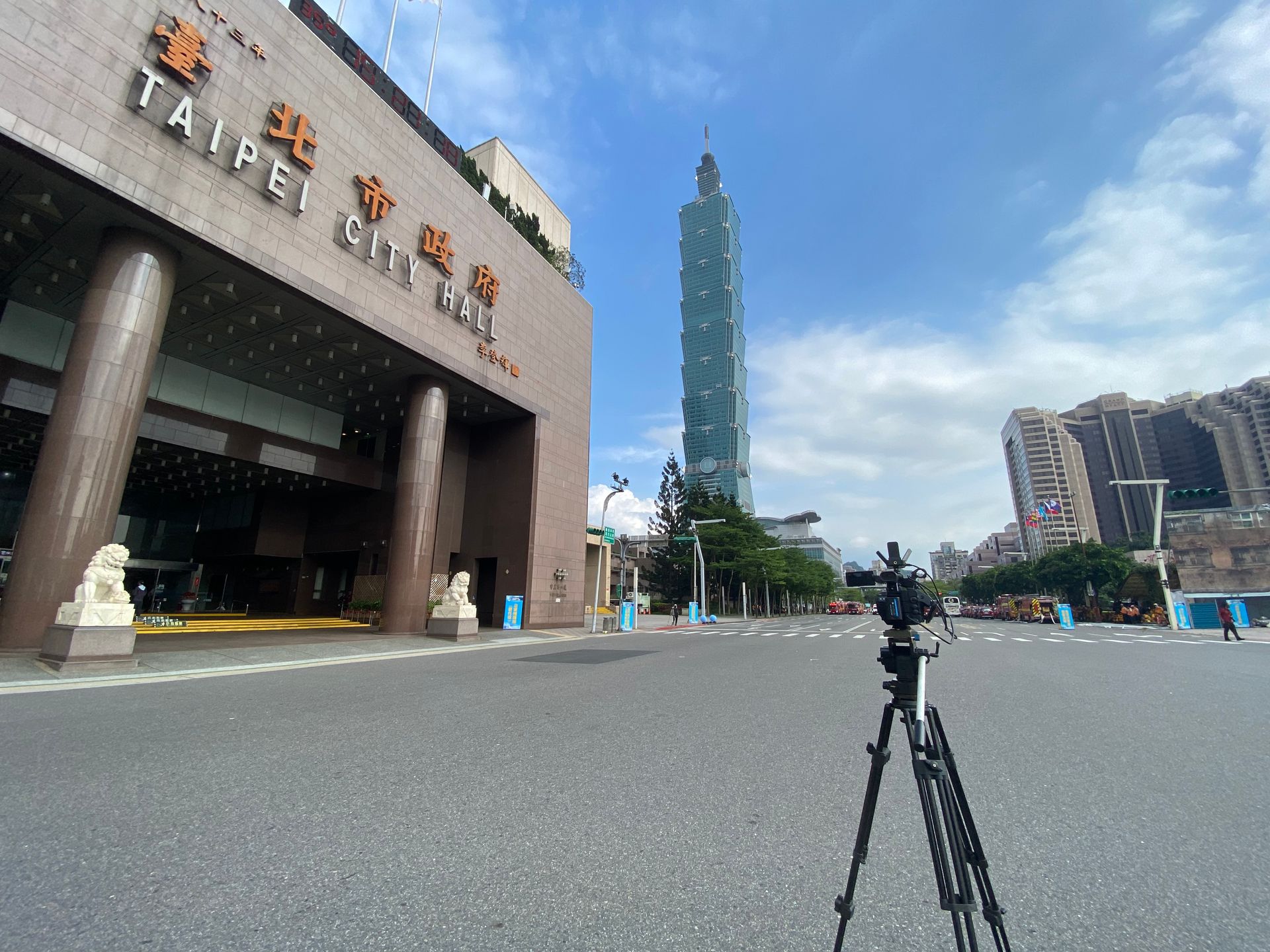 背景中是台北市政廳和台北101大樓。路上的相機三腳架。陽光明媚的日子。