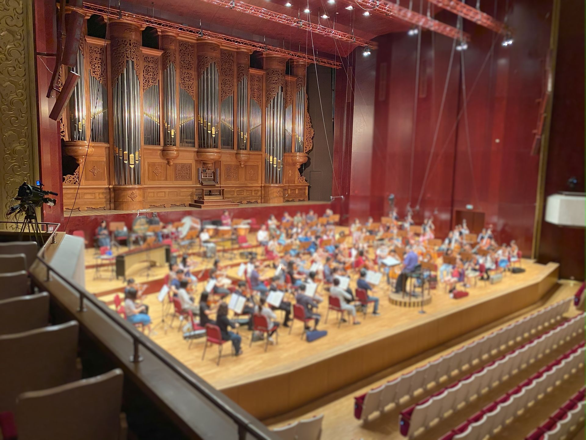 一支管弦樂團在舞台上表演，背景是一架大型管風琴；場景是一座禮堂。