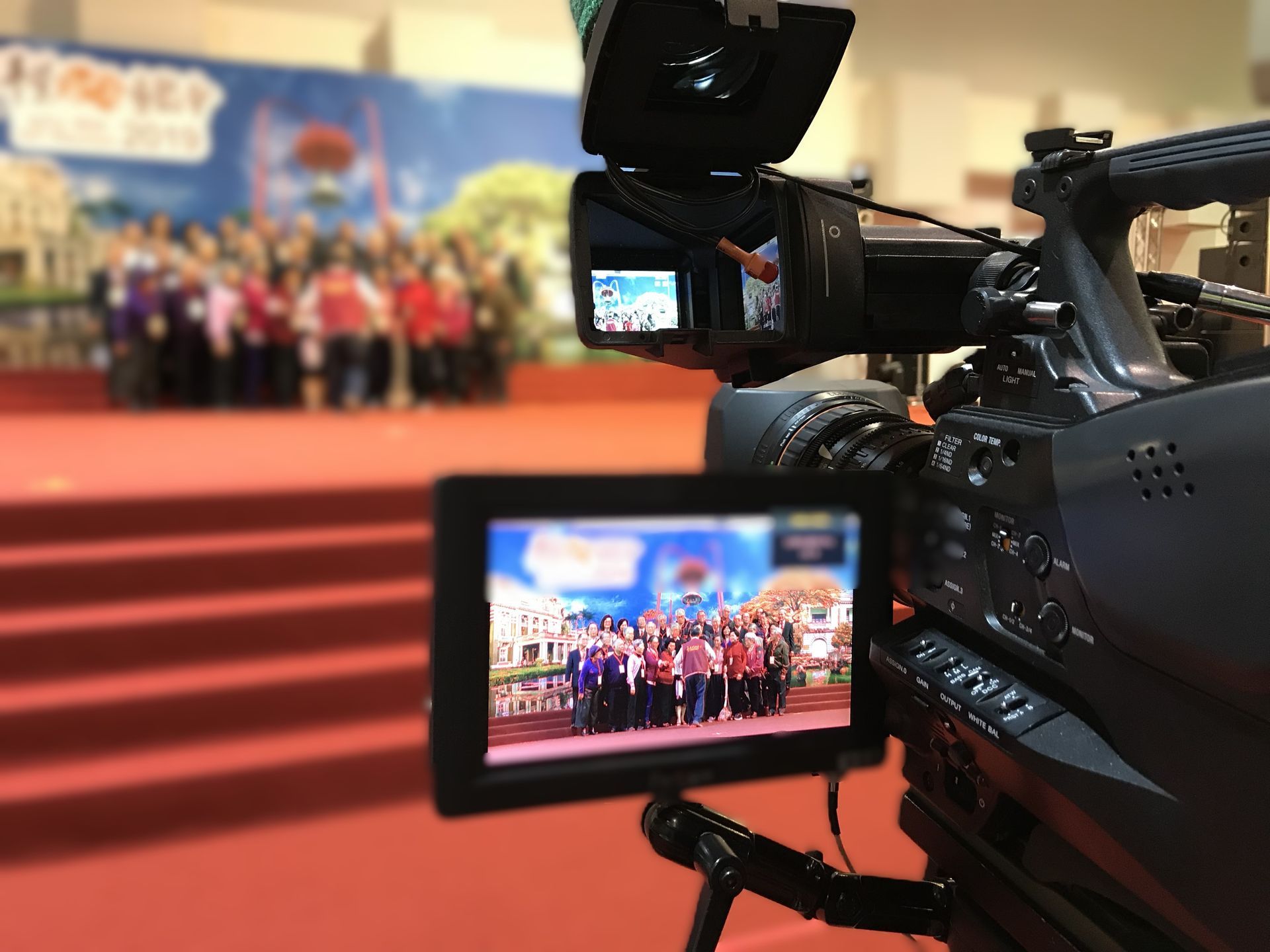 攝影機拍攝鋪著紅地毯的舞台上的一群人。