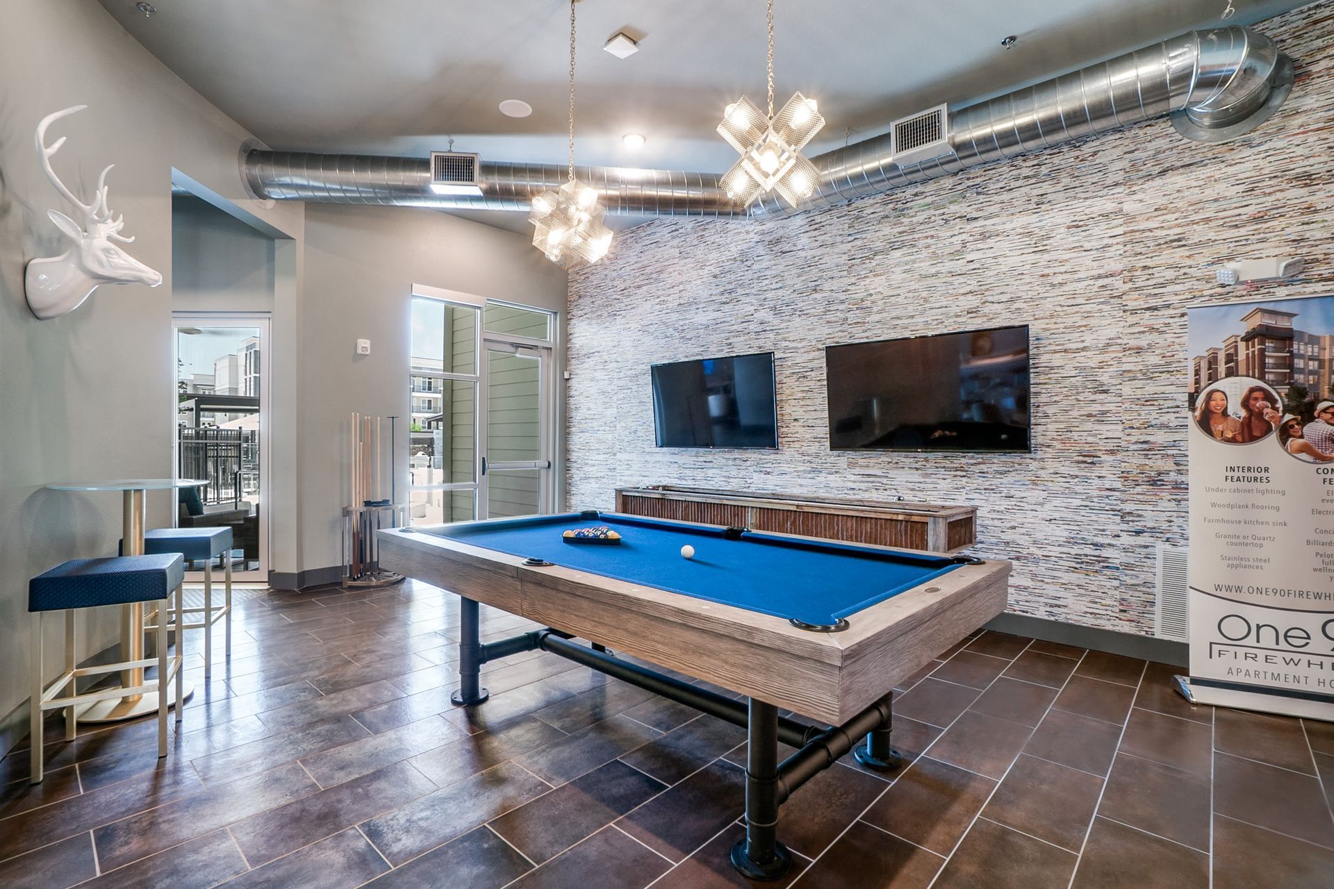 Indoor amenity room with a pool table, stone accent wall, and wall-mounted TVs.