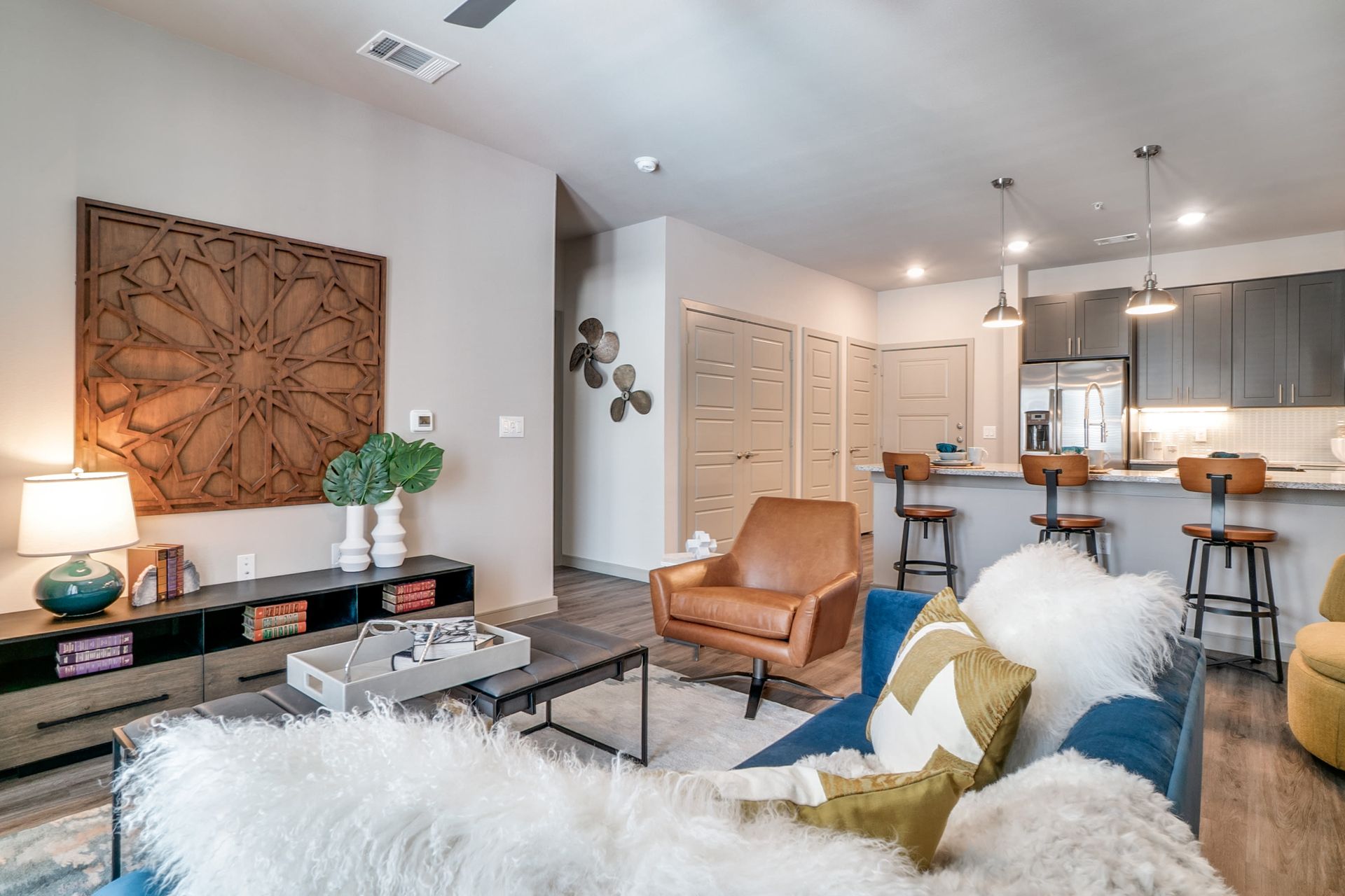 Open-concept living area with a blue sofa, leather armchair, coffee table, and a kitchen island with bar stools.