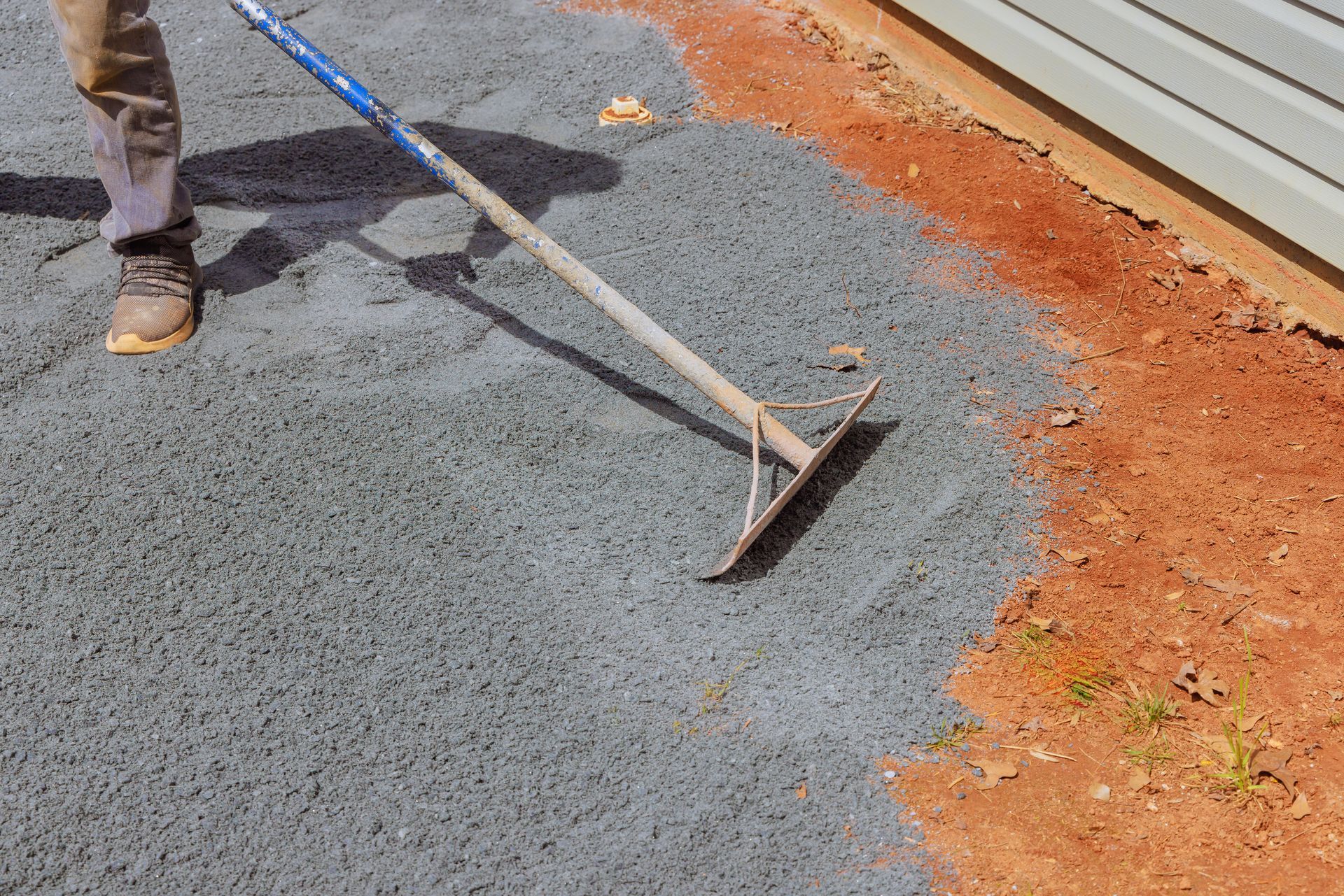 A person is raking a pile of asphalt on the ground.