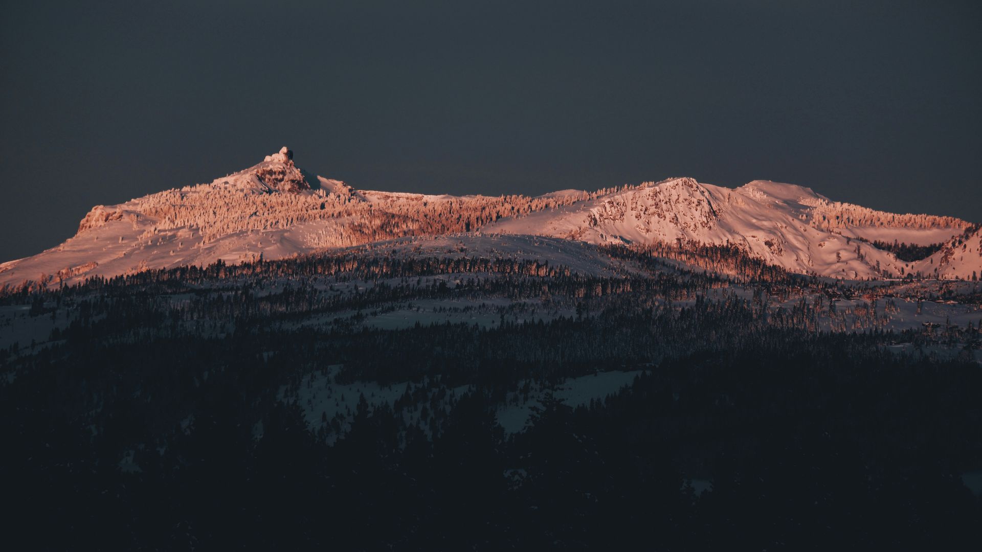 Snow-covered mountain ridge glowing pink at sunset against a dark sky