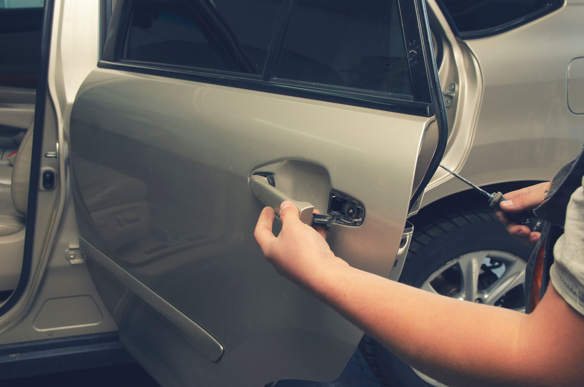 A locksmith works with the door lock and handle of a car with a screwdriver.