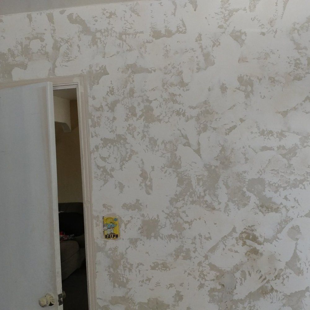 Partially painted room with peeling white walls and an open door to a dim hallway