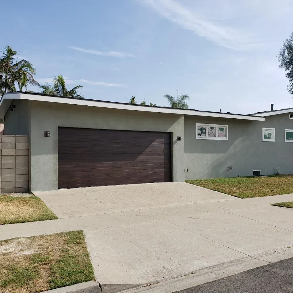 Modern single-story house with a dark garage door, light gray exterior, and a concrete driveway