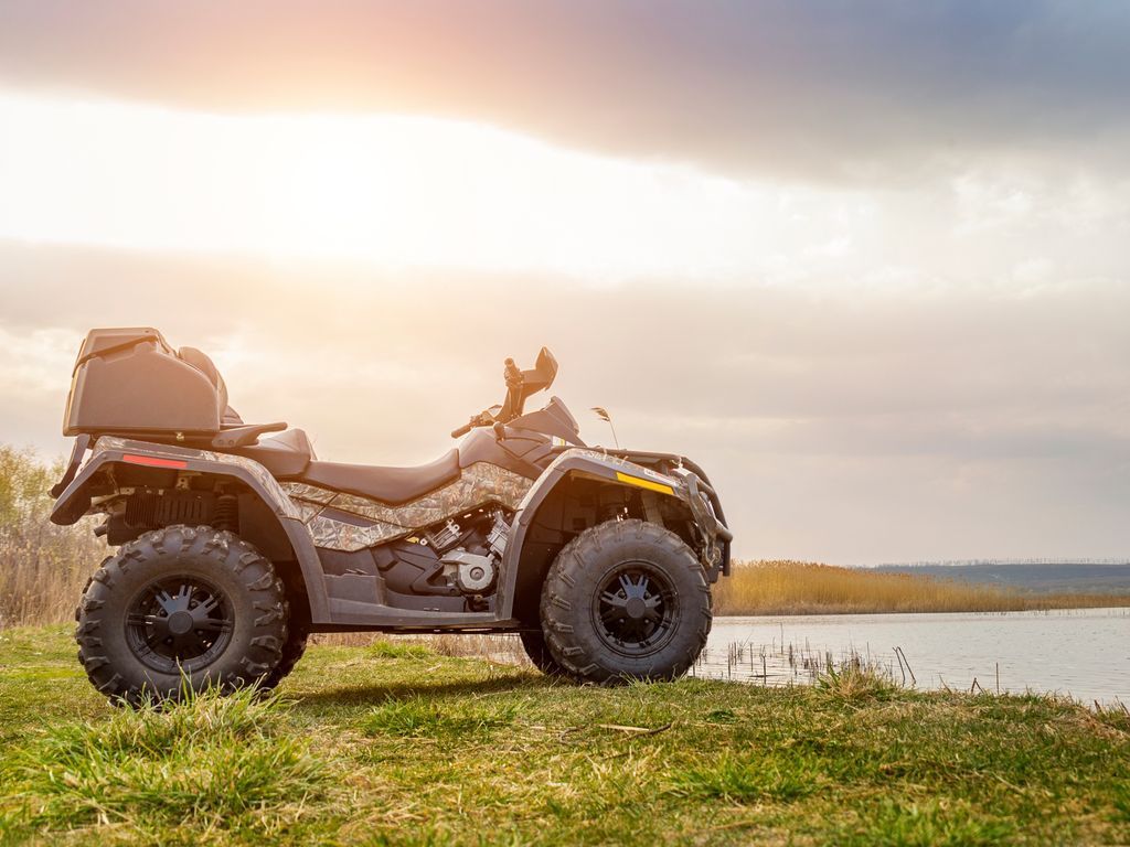 A four wheeler is parked on the grass near a lake.