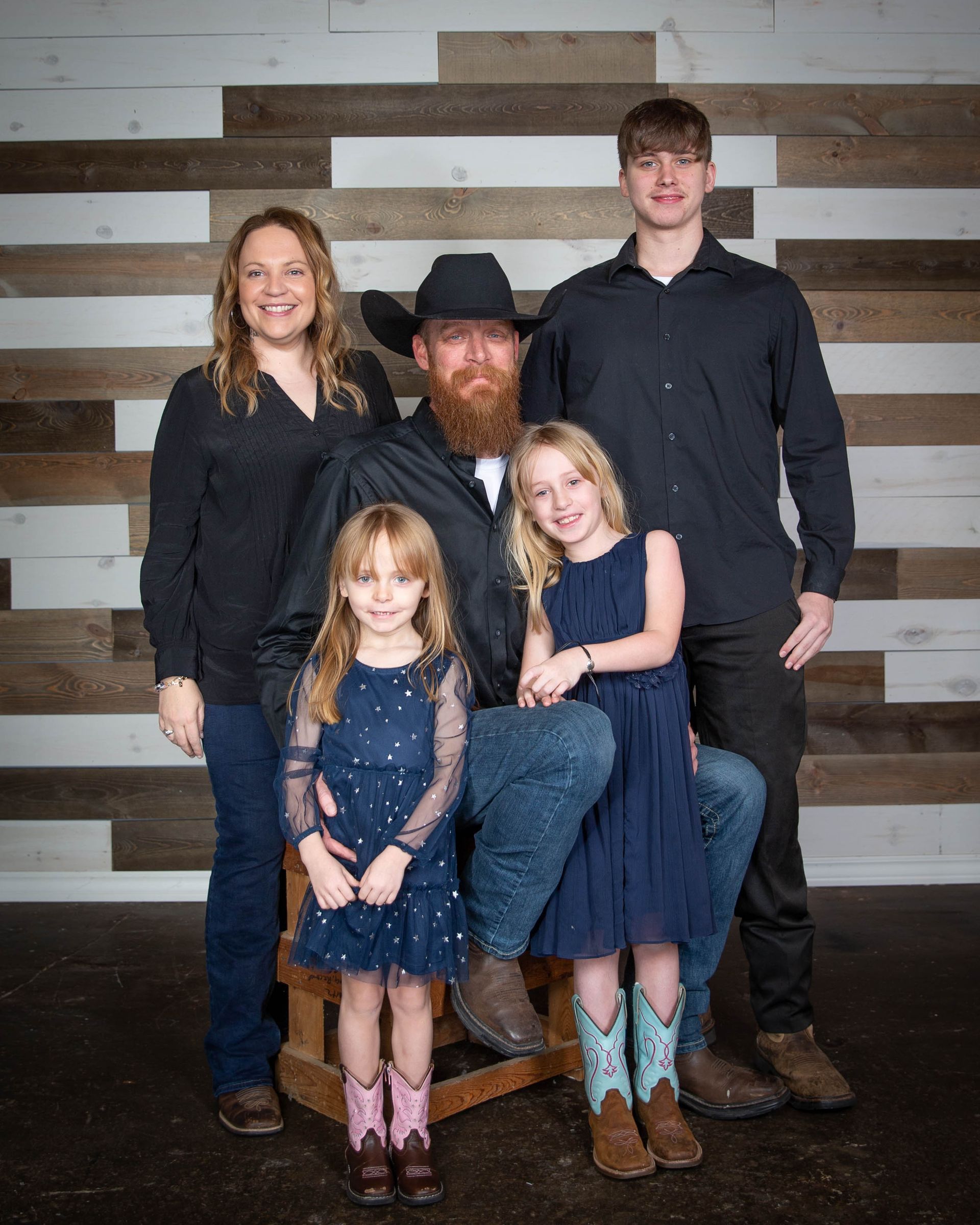 Family portrait; father in cowboy hat with children, mother, and teen boy against wood backdrop.