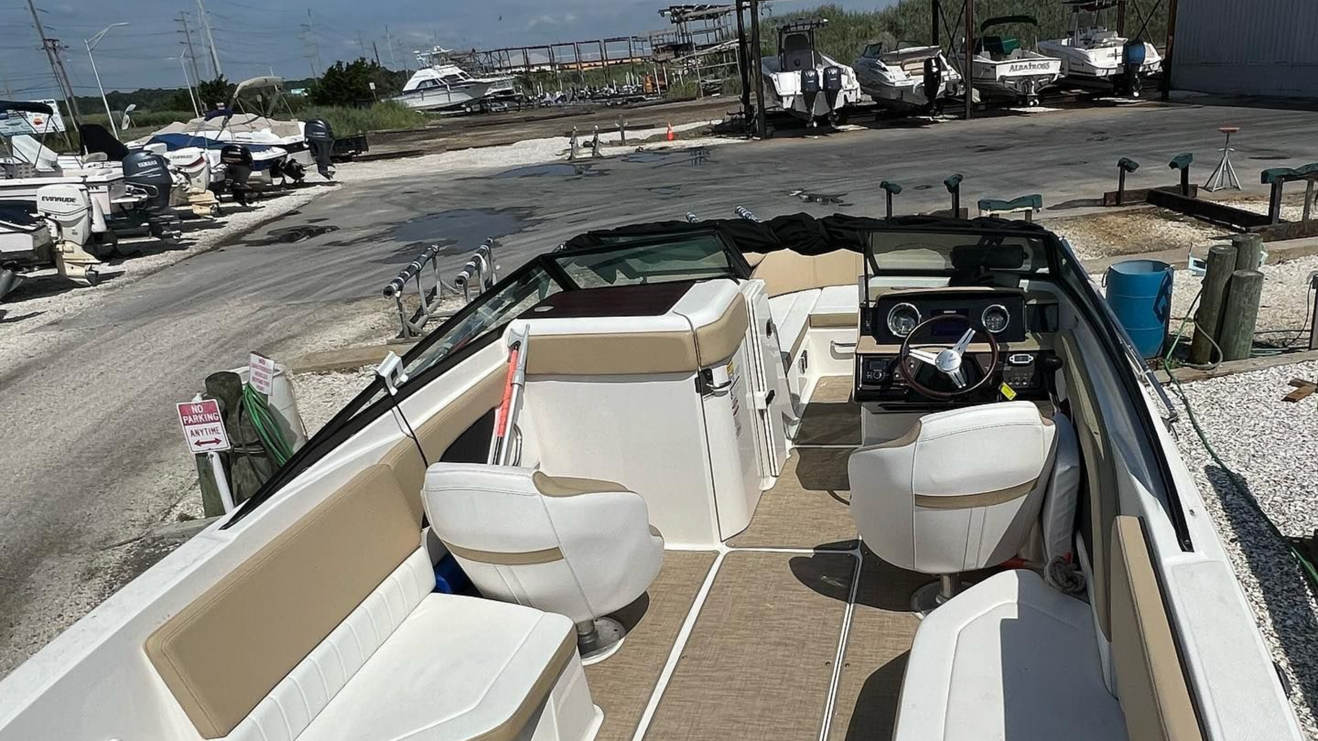 Empty white boat interior on a gravel lot, with docked boats and buildings in the background.