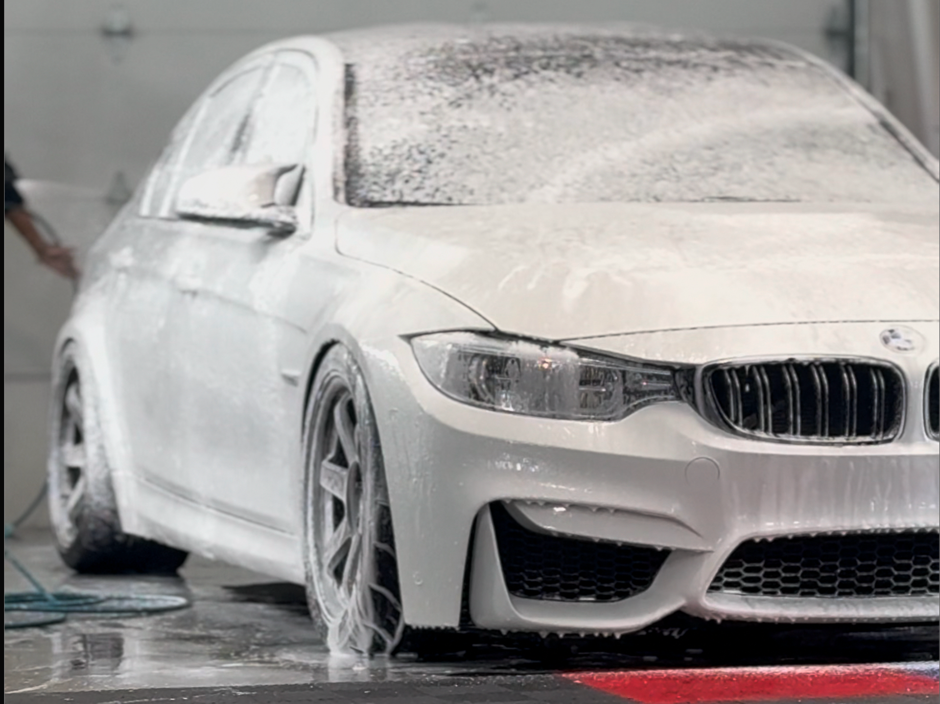 A man is washing a white sports car in a garage.